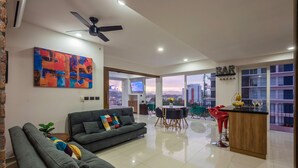 A modern living room with a grey sofa, a colorful abstract painting, and a dining area with a bar. - Stylish Golden Beach View Apartmen (Puerto Vallarta)