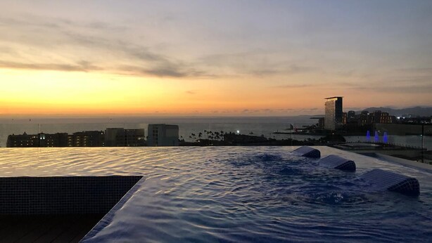 A rooftop infinity pool with a city skyline and ocean view at sunset. - Stylish Golden Beach View Apartmen (Puerto Vallarta)