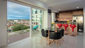 A modern kitchen with a stainless steel refrigerator, wooden cabinets, and a glass dining table with black chairs. - Stylish Golden Beach View Apartmen (Puerto Vallarta)