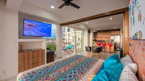 A modern bedroom with a large bed, a ceiling fan, a TV, and a balcony with a view of the city. - Stylish Golden Beach View Apartmen (Puerto Vallarta)