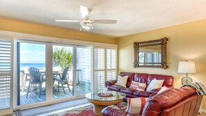 A living room with a glass coffee table, a leather sofa, and a ceiling fan.