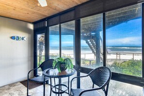 A room with a large window overlooking a beach, a small table with chairs, and a potted plant.