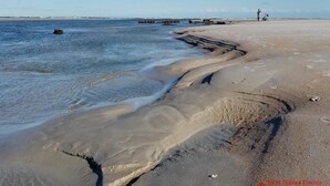 A beach with clear water, a sandy shore, and a few people in the distance.