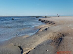 Une plage à l’eau claire, avec un rivage sablonneux et quelques personnes visibles au loin.