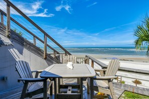 A beachside patio with a table and chairs, overlooking the ocean.