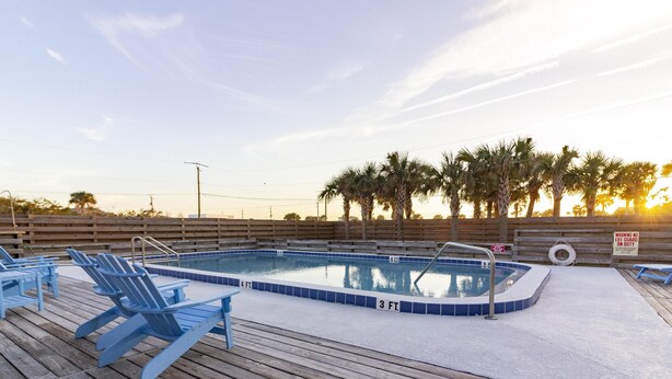A wooden deck with a swimming pool, lounge chairs, and palm trees.