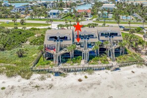 A beachfront property with a central building featuring multiple balconies and a staircase leading to a lower level.