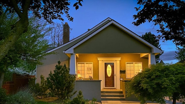 Een gelijkvloers huis met een veranda, een zichtbare schoorsteen en een verzorgd gazon.