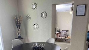 Un coin repas comprenant une table ronde et quatre chaises, un vase avec des fleurs séchées et des œuvres d’art décoratives accrochées au mur.