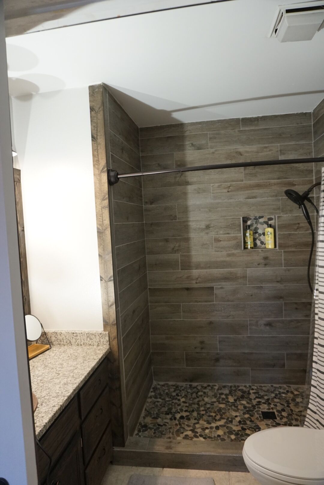 A shower with a wooden wall, a towel rack, and a shelf with toiletries.