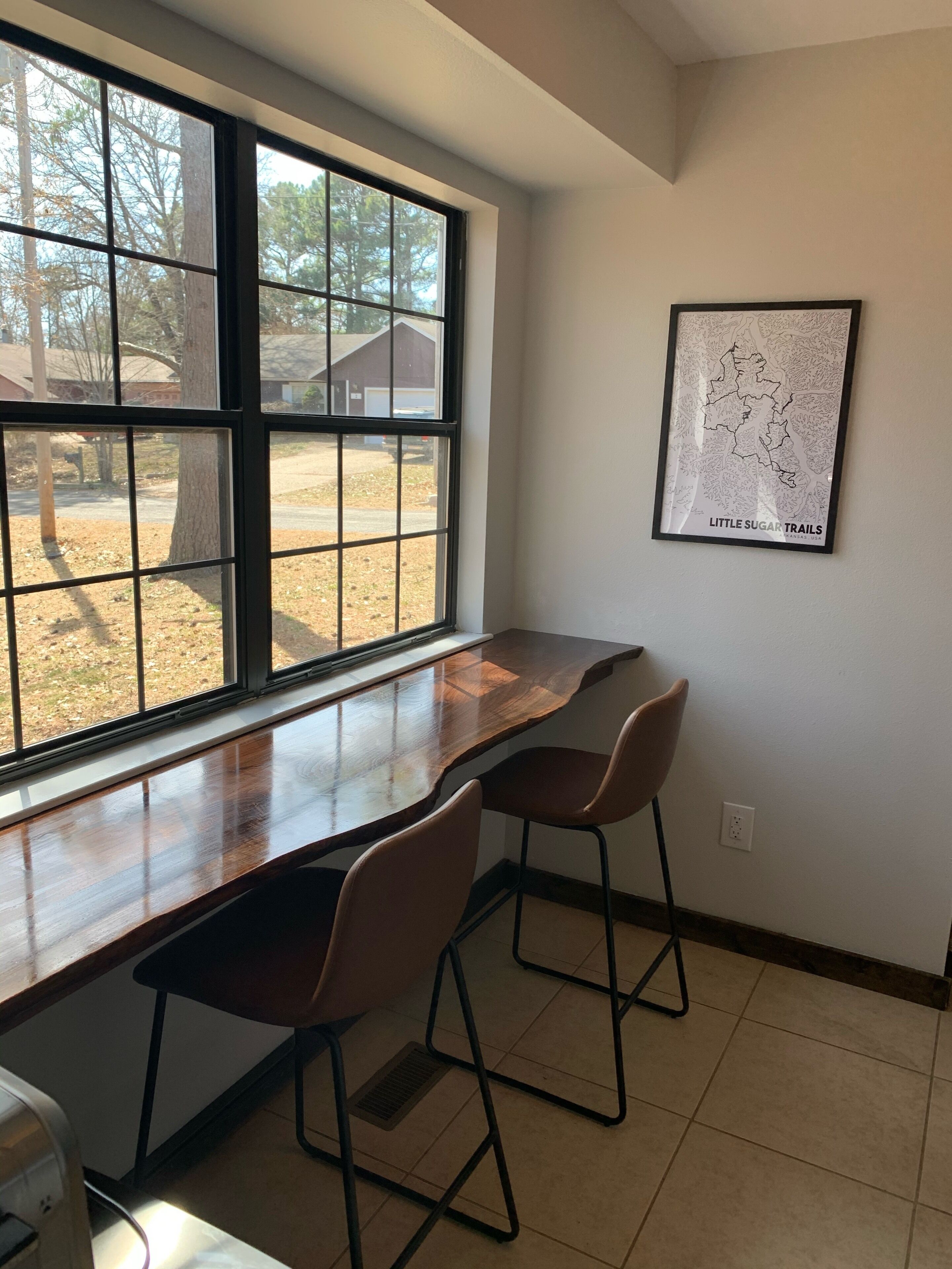 A room with a large window, a wooden desk, two chairs, and a map on the wall.
