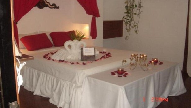 Una cama bien hecha con almohadas rojas, un dosel blanco y una mesita de noche con una planta pequeña y un objeto decorativo.