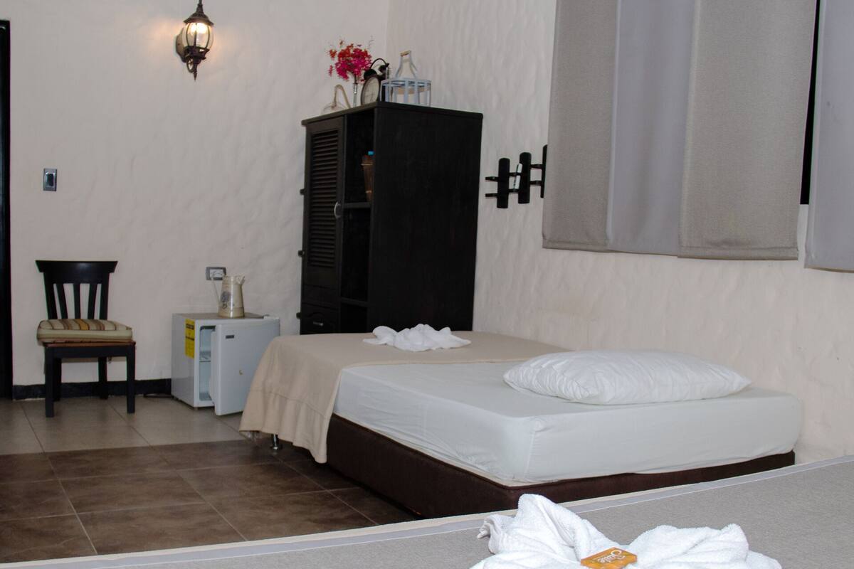 Ein Hotelzimmer mit zwei Betten, einem kleinen Tisch mit Stuhl, einem Schrank und einer Wandleuchte.