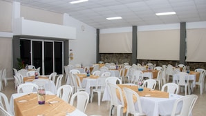 Salão de festas com várias mesas e cadeiras dispostas em fileiras.