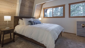 Un dormitorio con techo de madera, una cama con ropa blanca, dos lámparas de noche y un aparador con cajones.