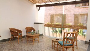 A balcony with wicker furniture and a small table, featuring a view of a brick building and greenery. - Captivating 4 -bed Apartment in Bellagio Historic (Bellagio)