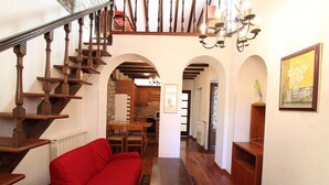 A spacious living area with a red sofa, wooden staircase, and a kitchen visible through an archway. - Captivating 4 -bed Apartment in Bellagio Historic (Bellagio)