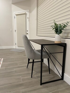 Una habitación con una mesa de madera oscura, una silla gris, una puerta blanca y una planta en maceta sobre la mesa.