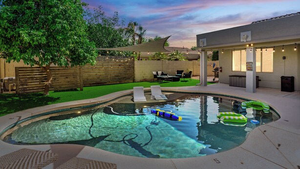A swimming pool with lounge chairs, a tree, and a building with lights. - Central Scottsdale w/heated pool, BBQ, EV charging (Scottsdale)