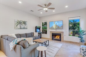 Ein Wohnzimmer mit einer Couch, einem Couchtisch, einem Kamin, einem Deckenventilator und einem Fernseher.