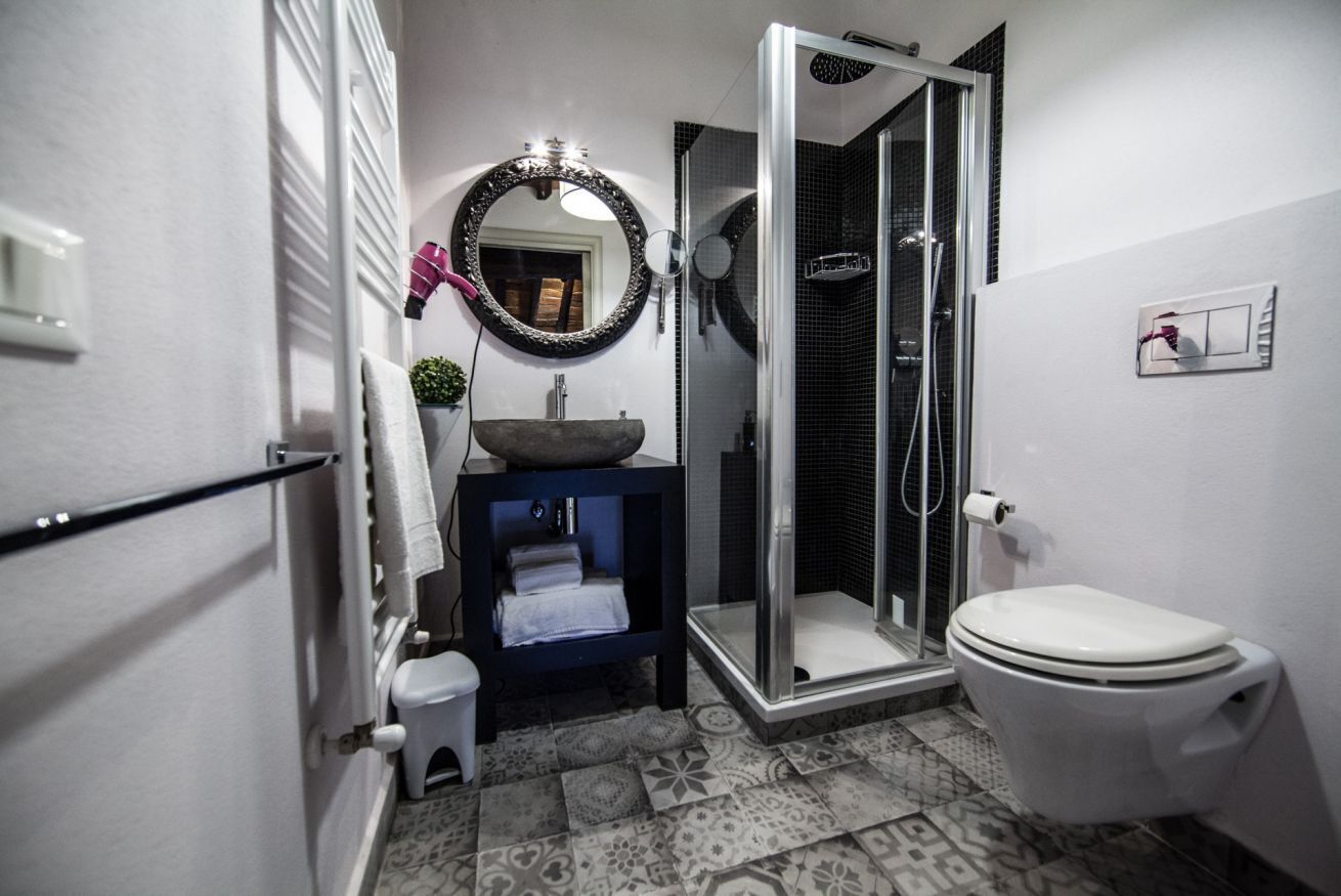 A bathroom with a toilet, a sink with a bowl, a mirror, a shower with a glass door, and patterned floor tiles.