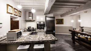 Una cocina con una isla central, un refrigerador, un horno y un microondas. Hay taburetes en la isla, y el techo tiene vigas a la vista.
