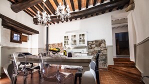 Un comedor con techo de madera, sillas transparentes, una isla central con frutero y una pared de piedra.