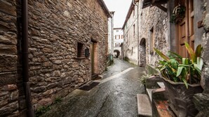 Una estrecha calle empedrada flanqueada por edificios, suelo mojado y una puerta de madera a la derecha.