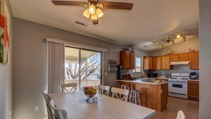 A modern kitchen with wooden cabinets, a central island, and a dining area with a table and chairs. - This One's Better-More To Do-More Modern-More Fun!!! (Prescott Valley)
