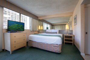 Une chambre d’hôtel avec un grand lit, un téléviseur posé sur une commode, un bureau et une fenêtre avec des rideaux.