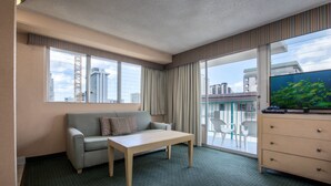 Een hotelkamer met een bank, een tafel, een kapstok en een groot raam met gordijnen.