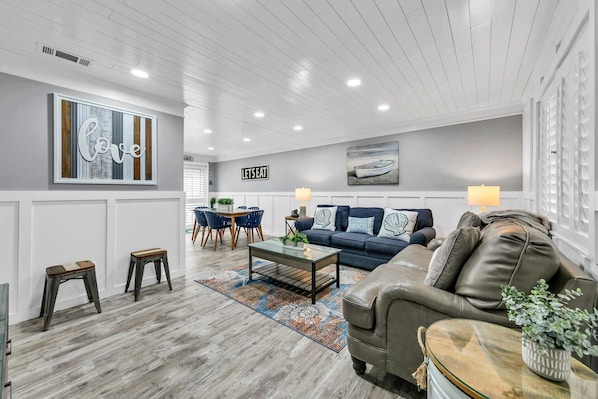A living room with a gray couch, a blue sofa, a coffee table, and a dining area with a table and chairs. - Southbay by the Gulf 72- Private Patio | Walk to the Beach (Destin)
