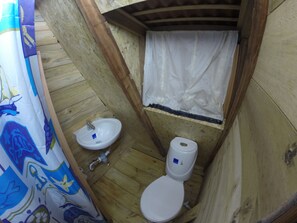 Une petite salle de bain aux murs lambrissés, équipée de toilettes, d’un lavabo et d’un rideau de douche.