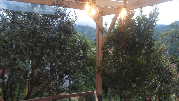 Un bain à remous surmonté d’une pergola en bois, entouré d’une végétation luxuriante et avec une chaîne de montagnes en toile de fond.