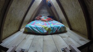 Une petite chambre mansardée, chaleureuse et accueillante, avec un plafond en pente et des murs en bois.