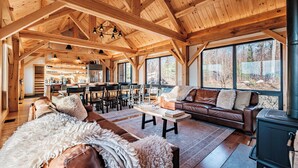 A spacious living area with a large wooden ceiling, a cozy fireplace, and a view of the outdoors through large windows.
