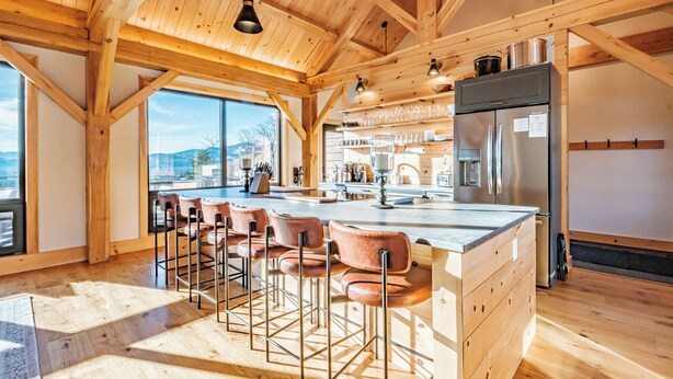 A spacious kitchen with wooden beams, a large island with bar stools, and a stainless steel refrigerator.