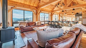 A spacious living area with a large wooden ceiling, a fireplace, leather sofas, and a view of the mountains.