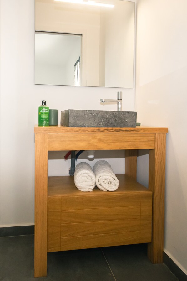 A wooden vanity with a gray sink, a mirror, and two rolled towels. - Villa Caribbean'ZEN, with a private pool (97170 PETIT BOURG)