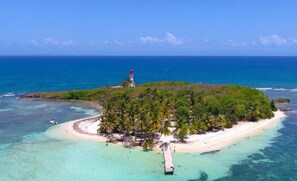 An aerial view of a tropical island with a lighthouse, clear turquoise waters, and a sandy beach.