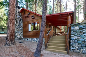 A cabin with a stone foundation, wooden exterior, and a staircase leading to a covered porch.