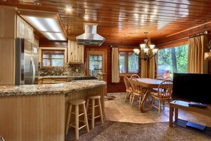 A kitchen with a central island, wooden cabinets, a stainless steel refrigerator, and a dining area with a table and chairs.
