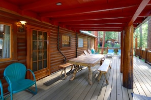 A wooden cabin with a covered porch, a table, benches, and chairs.