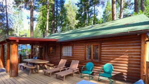 Una cabaña de troncos con una terraza, sillones de madera y una mesa de picnic.
