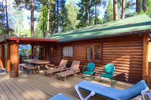 A log cabin with a deck, wooden lounge chairs, and a picnic table.