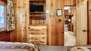Una habitación de madera con una cama, un televisor en un estante y una puerta que da a otra habitación.