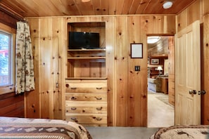 A wooden room with a bed, a TV on a shelf, and a door leading to another room.