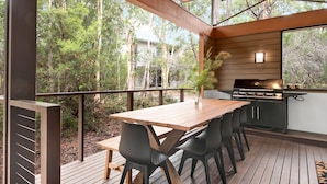An outdoor deck with a wooden table and chairs, a barbecue grill, and a view of the surrounding forest.