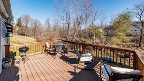 Une terrasse en bois, dotée de mobilier d’extérieur, d’un barbecue et offrant une vue sur les arbres et les collines.