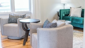 Ein Wohnzimmer mit zwei Sesseln, einem kleinen runden Tisch und einem grünen Sofa.